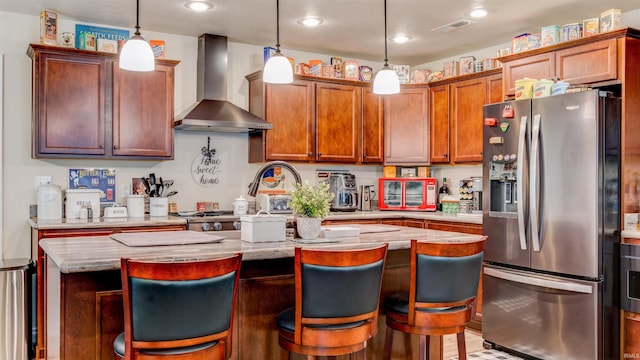 kitchen with stainless steel fridge with ice dispenser, a kitchen island, a breakfast bar area, wall chimney exhaust hood, and pendant lighting