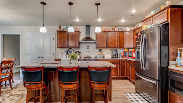 kitchen with wall chimney range hood, a kitchen island, light hardwood / wood-style floors, and stainless steel refrigerator with ice dispenser