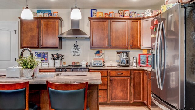 kitchen with wall chimney range hood, light hardwood / wood-style floors, stainless steel fridge, and pendant lighting