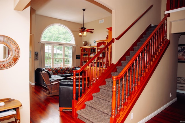 stairs featuring a high ceiling, dark wood-type flooring, and ceiling fan