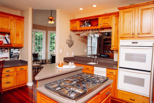 kitchen featuring ceiling fan, kitchen peninsula, white double oven, dark hardwood / wood-style flooring, and stainless steel gas cooktop