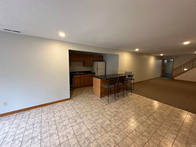 kitchen with light carpet, white refrigerator, a textured ceiling, sink, and a breakfast bar