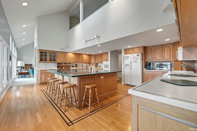 kitchen featuring white appliances, a kitchen island with sink, high vaulted ceiling, and light wood-type flooring