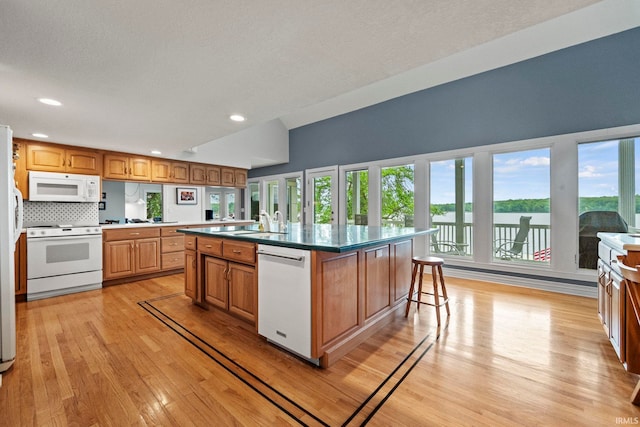 kitchen with light hardwood / wood-style floors, white appliances, an island with sink, backsplash, and sink