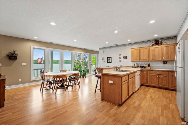 kitchen featuring a kitchen breakfast bar, light hardwood / wood-style flooring, white appliances, kitchen peninsula, and sink