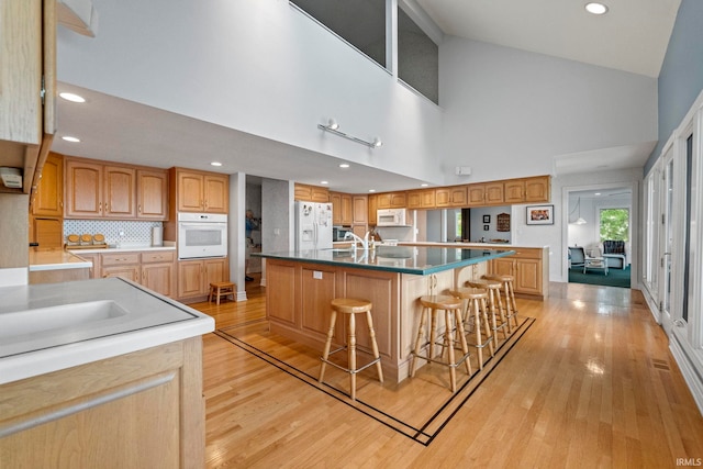 kitchen featuring light hardwood / wood-style floors, a kitchen bar, an island with sink, high vaulted ceiling, and white appliances