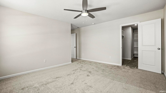 unfurnished bedroom with a walk in closet, a closet, ceiling fan, and dark carpet