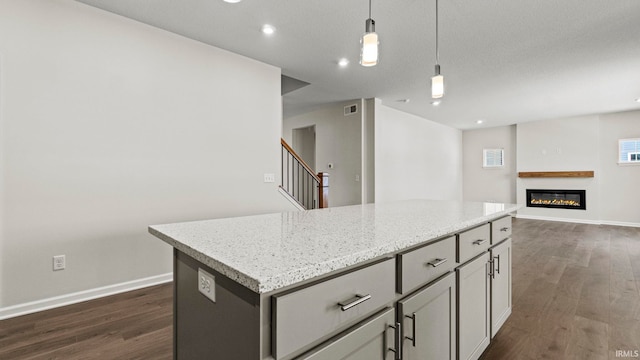 kitchen with a kitchen island, light stone counters, dark hardwood / wood-style floors, and pendant lighting