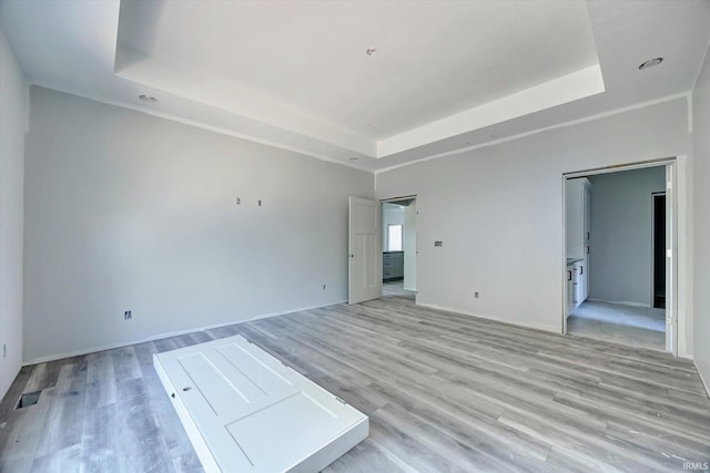 empty room featuring light wood finished floors, a raised ceiling, and baseboards