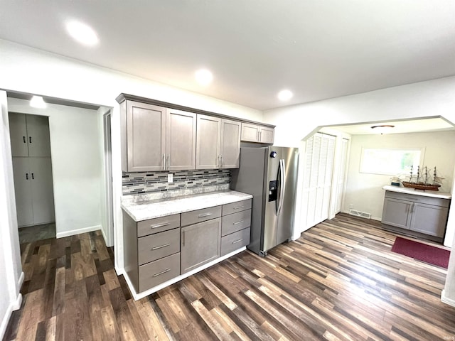 kitchen with tasteful backsplash, stainless steel refrigerator with ice dispenser, light stone counters, and dark hardwood / wood-style flooring