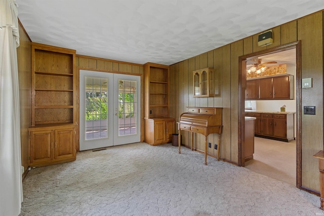 misc room featuring french doors, light colored carpet, ceiling fan, and wood walls