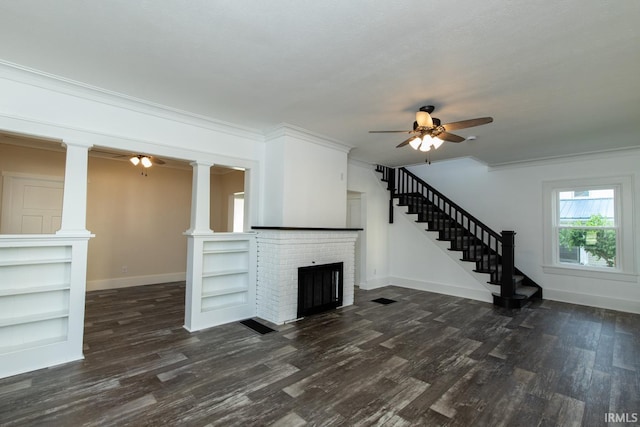 unfurnished living room featuring a brick fireplace, ceiling fan, decorative columns, and dark wood-type flooring