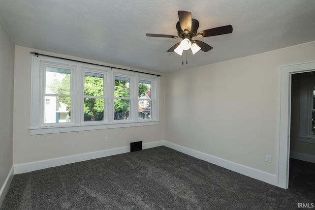 spare room featuring ceiling fan and dark carpet