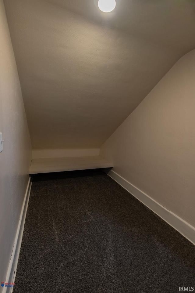 additional living space featuring vaulted ceiling and dark colored carpet