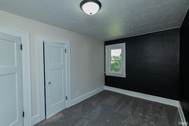 spare room featuring a textured ceiling and dark carpet