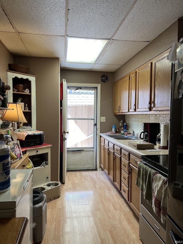 kitchen with a paneled ceiling, light wood-type flooring, sink, and stainless steel stove