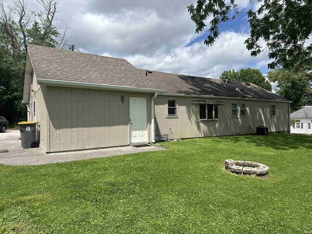 rear view of house with a fire pit, central AC unit, and a lawn