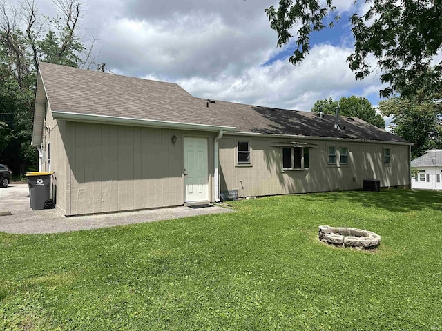 rear view of property featuring a fire pit, roof with shingles, and a lawn