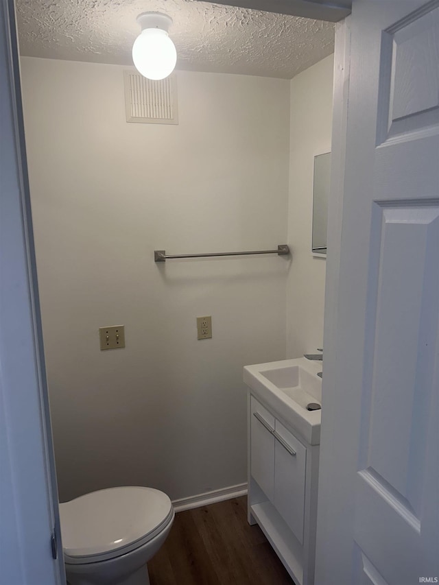 bathroom featuring a textured ceiling, toilet, wood finished floors, vanity, and visible vents