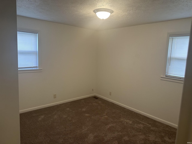 spare room with baseboards, dark carpet, and a textured ceiling