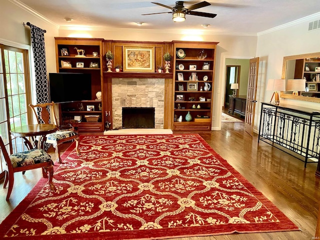 living room with a stone fireplace, ceiling fan, crown molding, and wood-type flooring