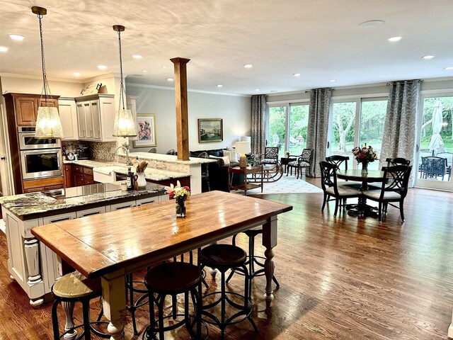 dining area featuring sink, ornate columns, dark wood-type flooring, and ornamental molding