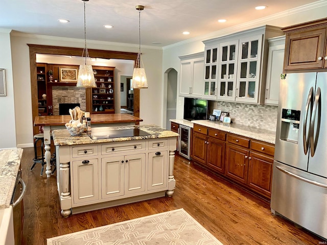 kitchen with a center island, crown molding, hanging light fixtures, a fireplace, and stainless steel fridge with ice dispenser