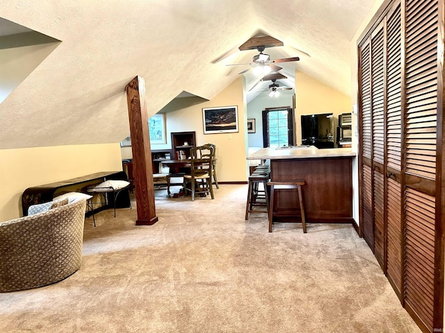 interior space featuring kitchen peninsula, lofted ceiling, a textured ceiling, a kitchen bar, and light carpet