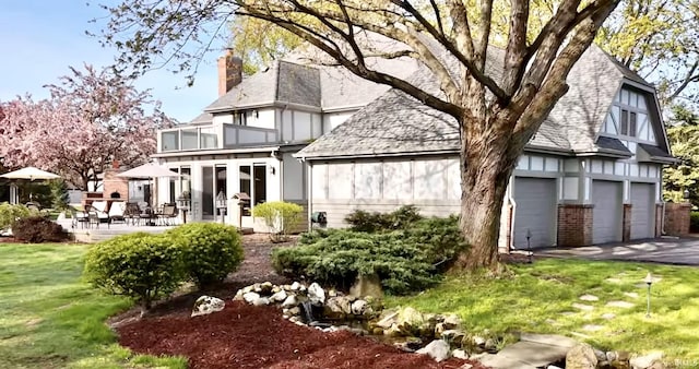 rear view of house featuring a lawn, a garage, a balcony, and a patio