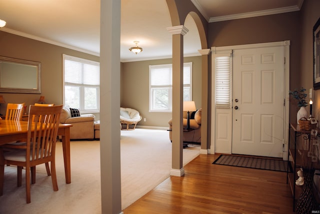 foyer entrance with baseboards, arched walkways, light wood-style floors, ornamental molding, and ornate columns