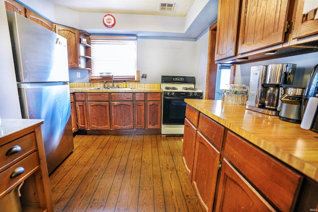 kitchen featuring light wood-type flooring, white range, stainless steel refrigerator, and sink