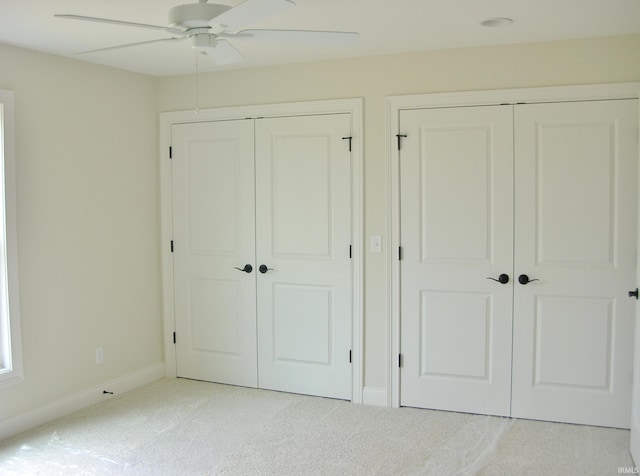 unfurnished bedroom featuring ceiling fan, light carpet, and multiple closets