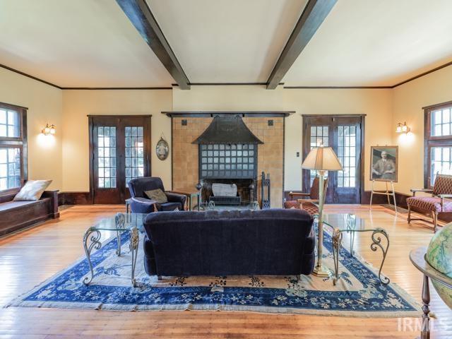 living room featuring wood-type flooring, beamed ceiling, a tiled fireplace, and french doors