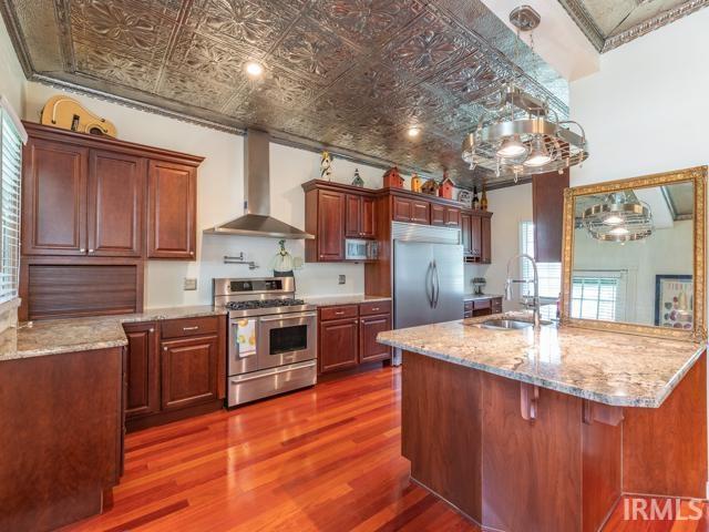 kitchen featuring wall chimney range hood, sink, dark hardwood / wood-style flooring, and appliances with stainless steel finishes