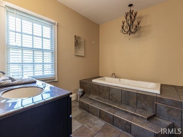 bathroom with a healthy amount of sunlight, tile flooring, tiled bath, and vanity