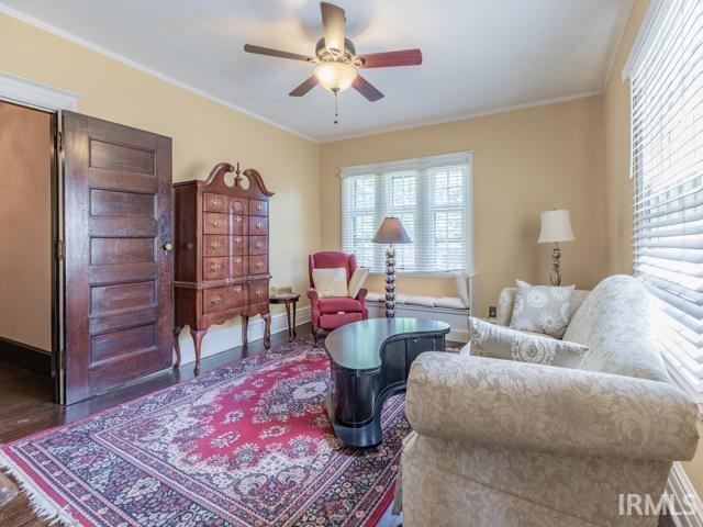 living room with dark wood-type flooring, ornamental molding, and ceiling fan