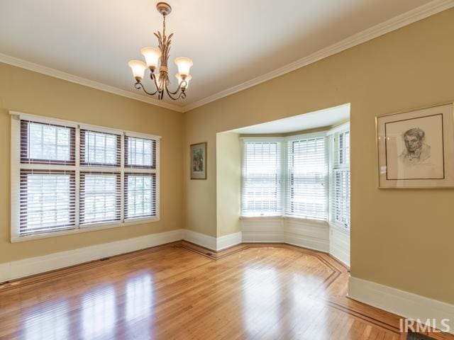 empty room featuring light hardwood / wood-style floors, a healthy amount of sunlight, crown molding, and an inviting chandelier