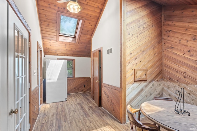 corridor featuring wood walls, vaulted ceiling with skylight, light hardwood / wood-style floors, and wooden ceiling