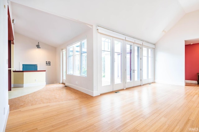 unfurnished living room featuring high vaulted ceiling, french doors, and light wood-type flooring