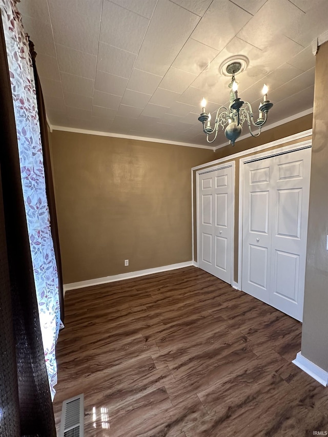 unfurnished bedroom featuring dark hardwood / wood-style flooring, an inviting chandelier, and crown molding