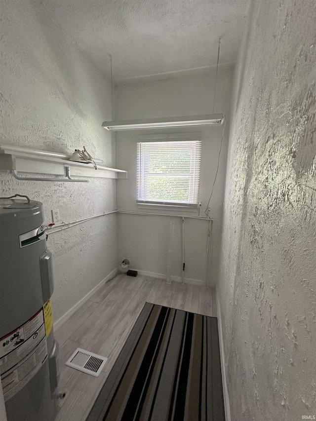 interior space with a textured ceiling, electric water heater, and light hardwood / wood-style flooring