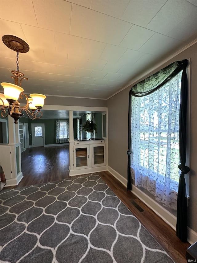 unfurnished living room with dark hardwood / wood-style flooring, crown molding, and an inviting chandelier