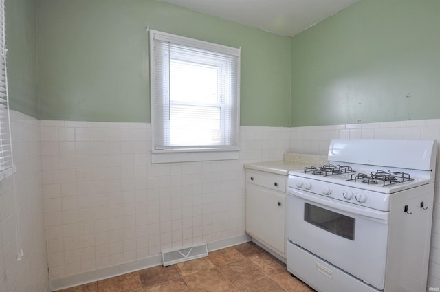 kitchen with white gas range oven, white cabinetry, tile walls, and light tile floors