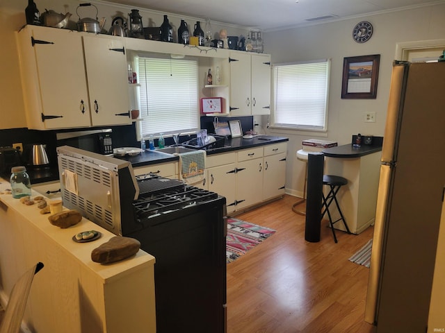 kitchen with stove, white cabinets, ornamental molding, light hardwood / wood-style floors, and stainless steel refrigerator