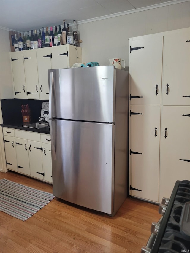 kitchen with sink, light hardwood / wood-style flooring, stainless steel fridge, crown molding, and white cabinets