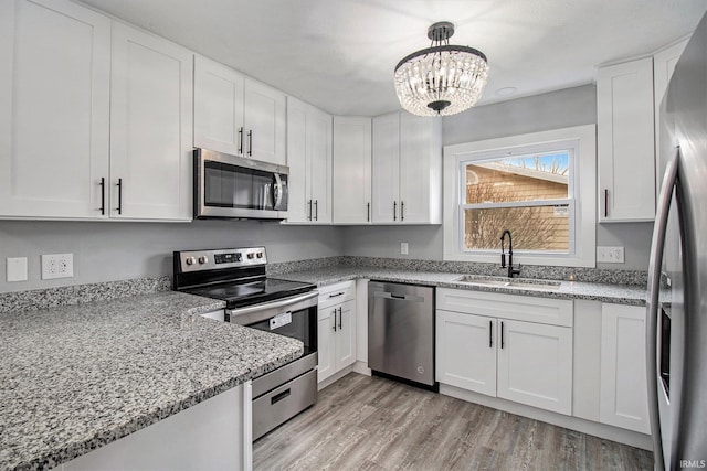 kitchen with appliances with stainless steel finishes, pendant lighting, sink, white cabinets, and light stone counters