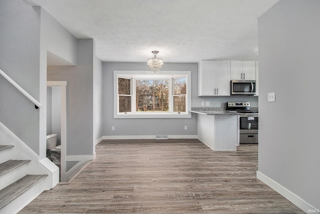 kitchen with stone counters, an inviting chandelier, appliances with stainless steel finishes, light hardwood / wood-style floors, and white cabinets