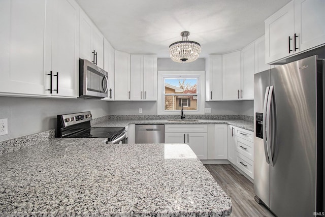 kitchen with sink, white cabinetry, hanging light fixtures, stainless steel appliances, and light hardwood / wood-style floors