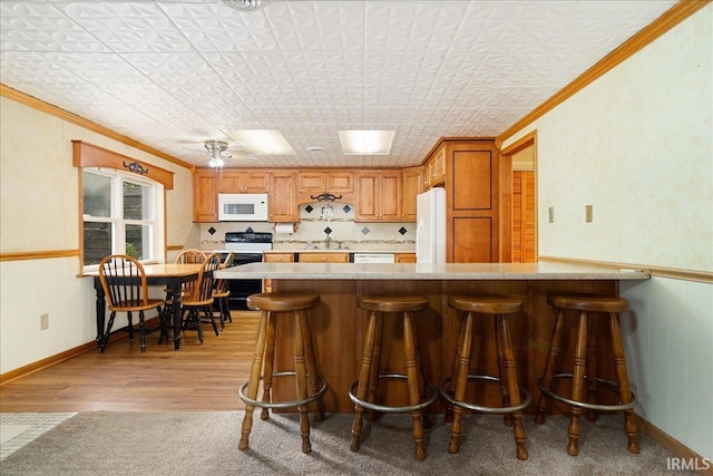 kitchen with a kitchen bar, light hardwood / wood-style floors, white appliances, and ornamental molding