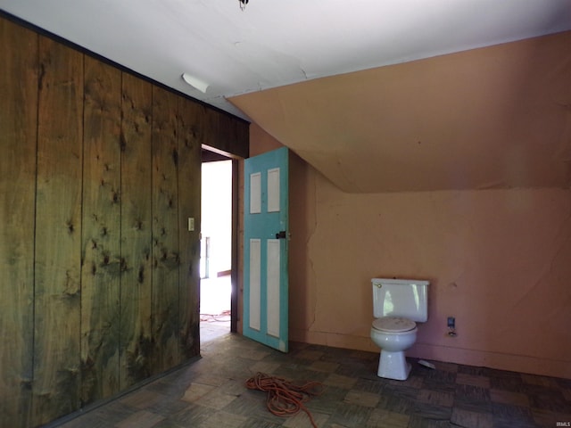 bathroom with wooden walls, vaulted ceiling, and toilet